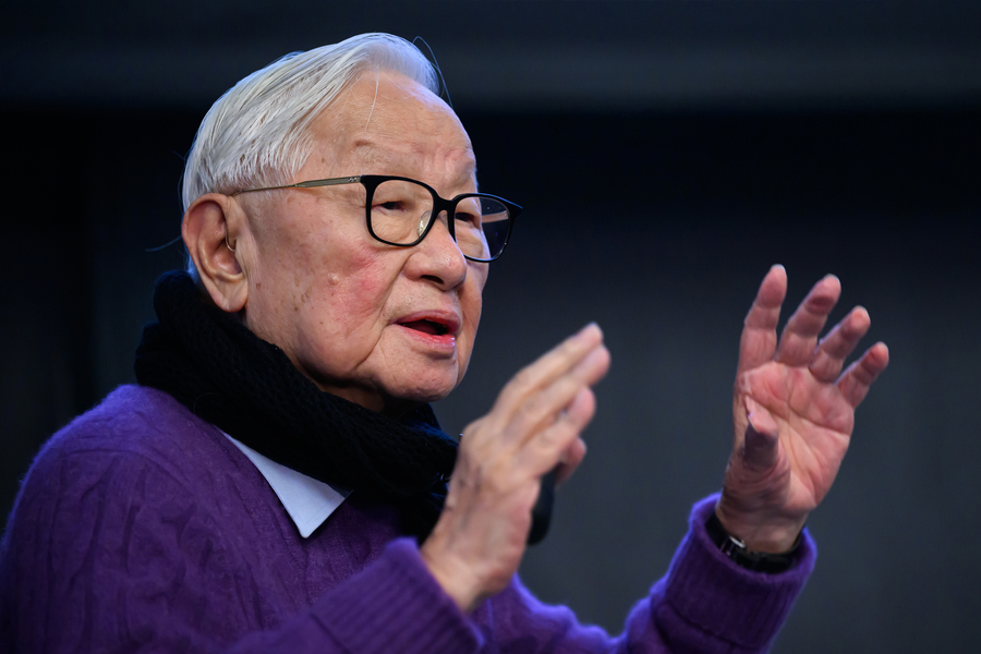 Closeup of Morris Chang as he gestures with his hands, while wearing a scarf and purple sweater.